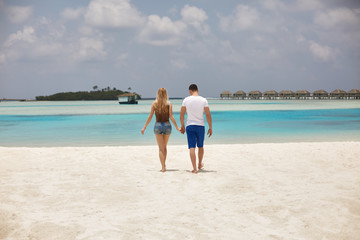Obraz premium Back view of couple holding hands and walking to the blue ocean lagoon on Maldives at luxury spa resort. Travel and honeymoon concept.