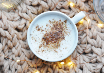 hot cappuccino with cinnamon on the knitted background with lights