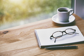 cup of fresh morning coffee with paper notebook, glasses and pen for writing