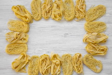 Frame of various uncooked pasta on white wooden background, overhead view. Flat lay, from above,...