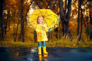 happy child girl with an umbrella and rubber boots in puddle on an autumn walk