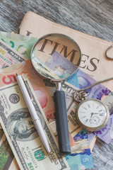 Different currency, pen, pocket clock and a magnifying glass