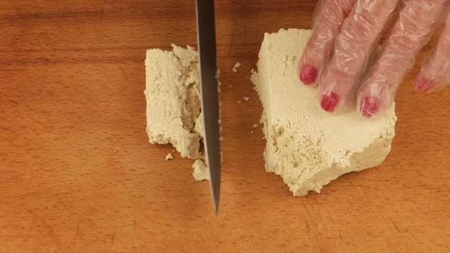 Woman cuts into pieces sesame halva on the wooden cutting board