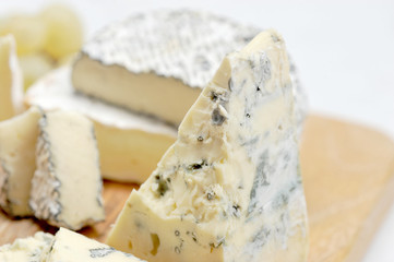Cheese plate: cheese with mold dorblu, camembert ashes, brie on a light wooden board. White background. Close-up. Macro photography.