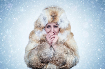 Frozen young woman in a fox fur coat warming hands, cold, snow, frost, blizzard