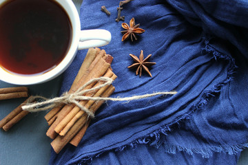 Autumn still-life. A Cup of hot tea yellow autumn leaf and spices, cinnamon sticks, anise, cloves on a blue scarf background. Warm warming drink, comfort, relaxation, relaxing drink.Tea, coffee with s