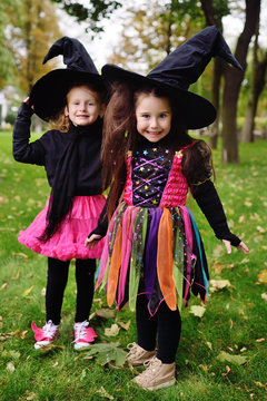 two cute baby girls in carnival costumes and big black witch hats during Halloween celebrations in the park