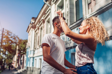 Mixed race couple in love listening to the music on phone and dancing on city street using earphones.