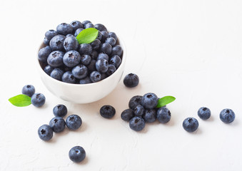 Fresh raw organic blueberries with leaf in white china bowl on white background. Macro close up