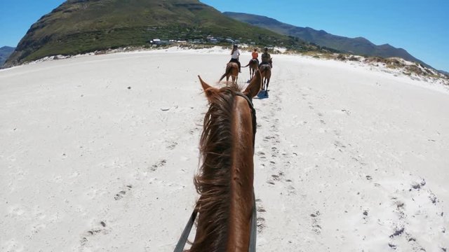 Group of horseback riders on beach, POV