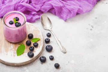 Fresh hommemade creamy blueberry yoghurt with fresh blueberries on vintage wooden board and silver spoon on stone kitchen table background