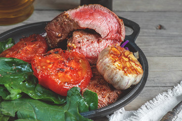 Steak with blood medium rare with a side dish of tomatoes and vegetables with spinach sauteed in a homemade pan on a wooden table.