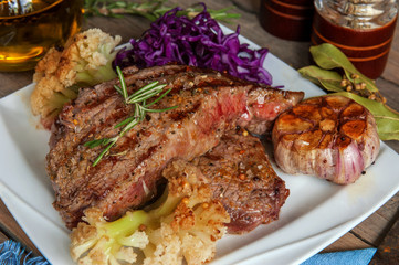 Steak with blood medium rare with a side dish of tomatoes and vegetables with spinach sauteed in a homemade pan on a wooden table.