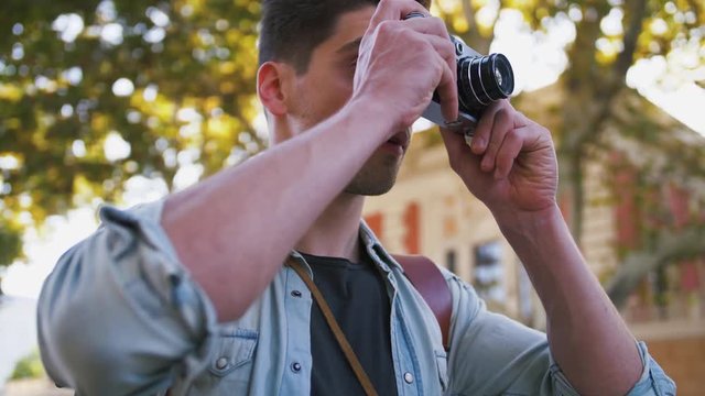 Close up shot of young attractive handsome man tourist with backpack taking photos on vintage camera in old city center, slow motion