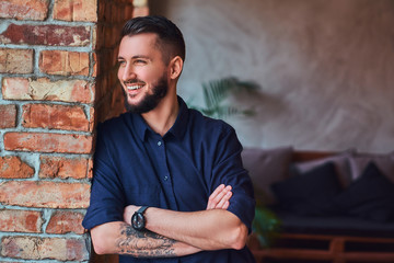 Happy bearded man standing with crossed arms near desktop in the office with loft interior.