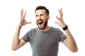Fototapeta premium close-up portrait of a young man with a beard, wearing a gray t-shirt, with an irritated expression, shouting in anger, hands in the air, isolated white background.