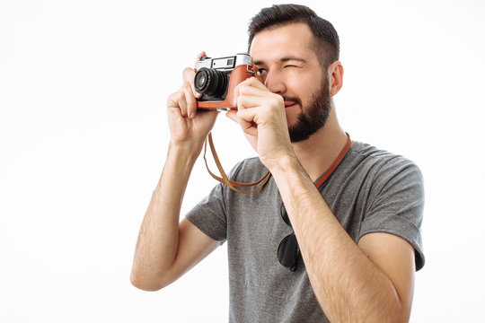 Portrait of a handsome photographer guy with a beard, taking pictures with a camera standing on a white background