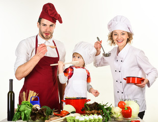Son, mother and father tasting ready soup with ladle and wooden spoons in kitchen at home. Dinner preparation. Healthy, vegetarian food. Homemade food. Cheerful parents teaching little son how to cook