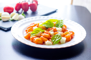 Gnocchi in tomato sauce with green fresh basil and mozzarella balls served on a plate. Italian recipe
