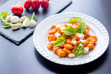 Gnocchi alla Sorrentina in tomato sauce with green fresh basil and mozzarella balls served on a...