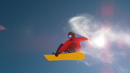 SLOW MOTION: Snowflakes shining in winter sun as snowboarder jumps over camera