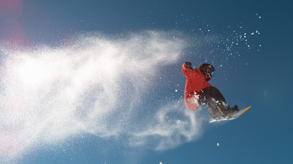 SLOW MOTION: Snowboarder jumping big air, snowflakes flying behind him in winter