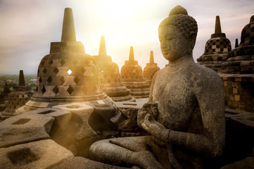 View of meditating Buddha statue and stone stupas against sunrise. Great religious architecture....