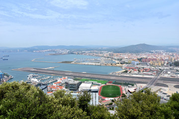 Daytime panoramic city view of busy harbor, air strip, soccer field, mountains, roads, and the beach