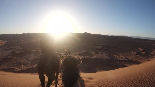 Sunset over camel riders in desert, POV
