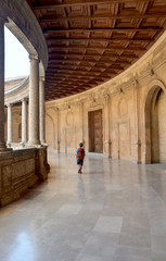 Fototapeta na wymiar Boy traveler with backpack walking through palace hallway with wood ceiling, columns, marble floors.