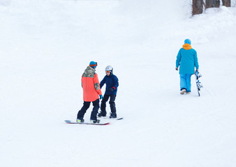 cute young boy in gray helmet and orange googles, in blue jacket snowboarding with instructor on white snow background. winter sport, active lifestyle concept.
