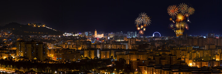 Panoramic aerial view to illuminated Malaga city at night and fireworks blowing in the sky