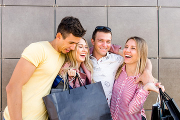 Four happy young friends with shopping bags hugging and rejoicing big sale