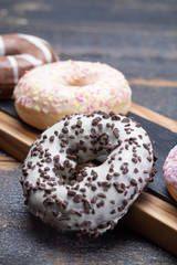 Colorful sweet glazed donuts from bakery on black wooden background close up