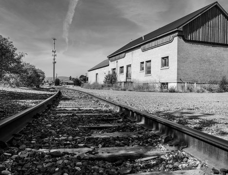 Black and White Image of abandoned railroad tracks make a turn by an abandoned railroad depot in the heart of a small town.