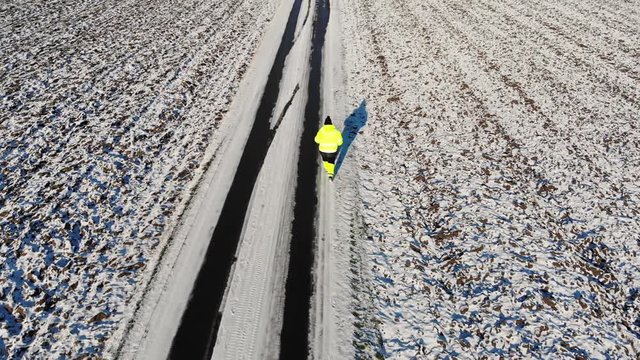 Man running in work clothes, White winter road by a feald.
Drone follow dolly shot.