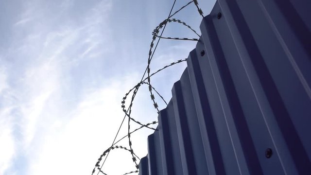 Metal fence with barbed wire on blue sky background  