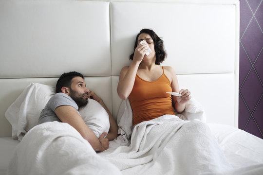 Young Woman Sneezing For Cold In Bed With Man