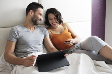 Happy Young Couple In Bed Buying Travel On Line