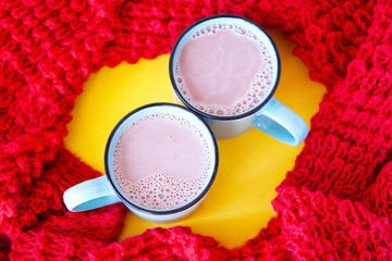 Two ceramic mugs with cocoa with milk, on a yellow background, surrounded by a red knitted scarf