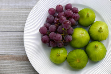 Green figs and purple grapes in a white bowl on an old wood table