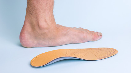 The left leg of an adult male with signs of foot disease next to the orthopedic insole. Means for the treatment of flat feet.