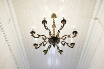 Vintage brass chandelier hanging from white wooden paneling ceiling
