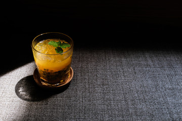 A glass of iced passion fruit drink in a glass cup on a wooden tray with black background
