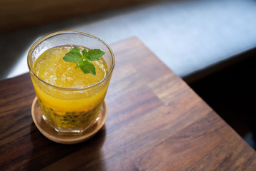 A glass of iced passion fruit drink in a glass cup on a wooden tray on a wooden table with blurred background