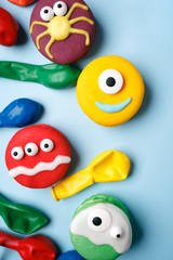 Heloween dessert: funny monsters made of biscuits macaroon with icing and candy eyes close-up on the table. vertical, party concept