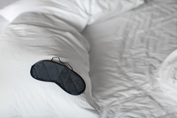 close up Sleep mask, bed with crumpled bed sheet, blanket and pillows after comfort duvet sleep waking up in the morning