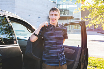 Happy teenager exiting his car and putting on his backpack as he arrives at school in the morning.