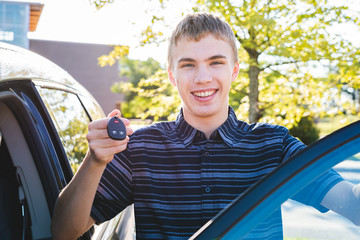 Happy teenager showing off his car keys as he stands next to his car. © Brian