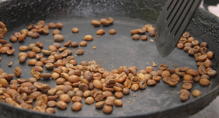Green coffee beans roasting on the black pan